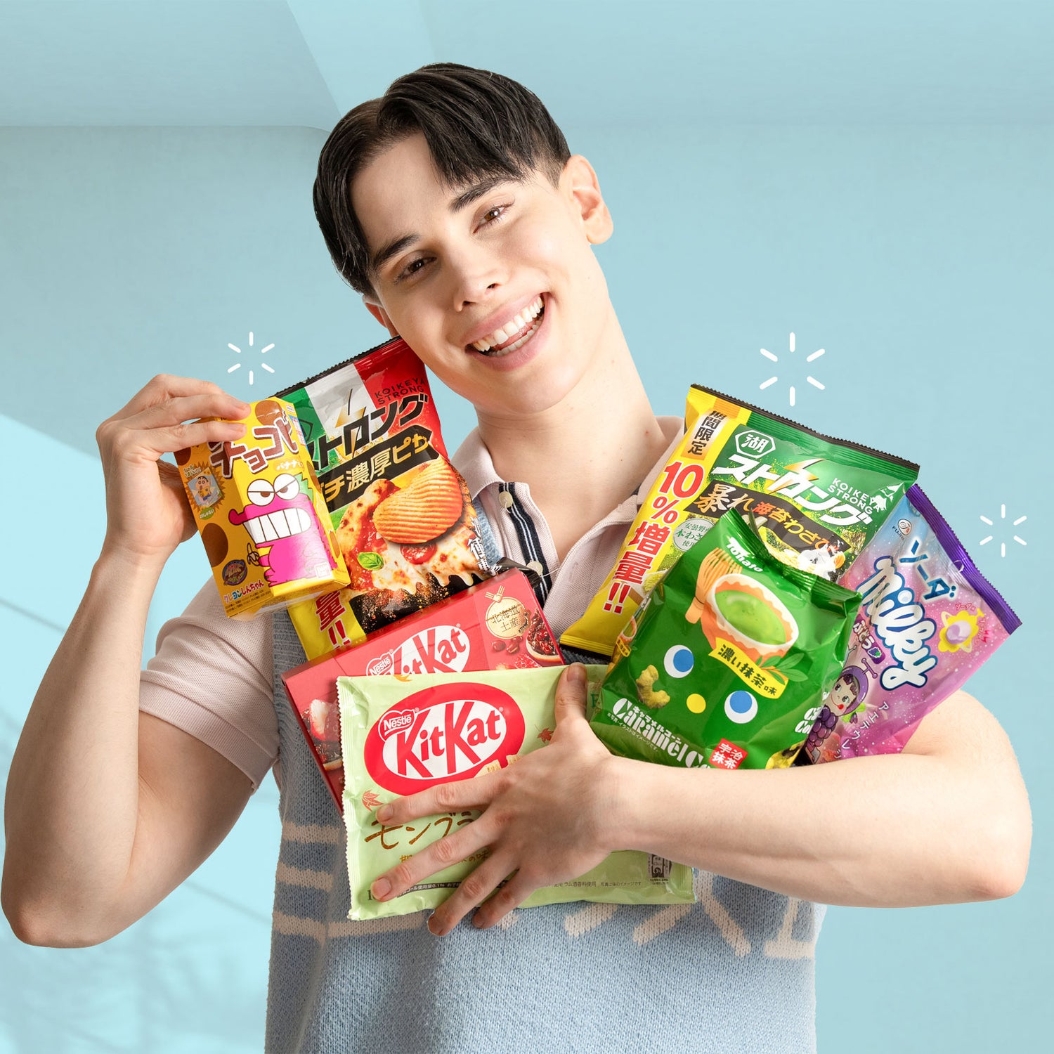 Person holding various KitKat and Japanese snack packages against a light blue background