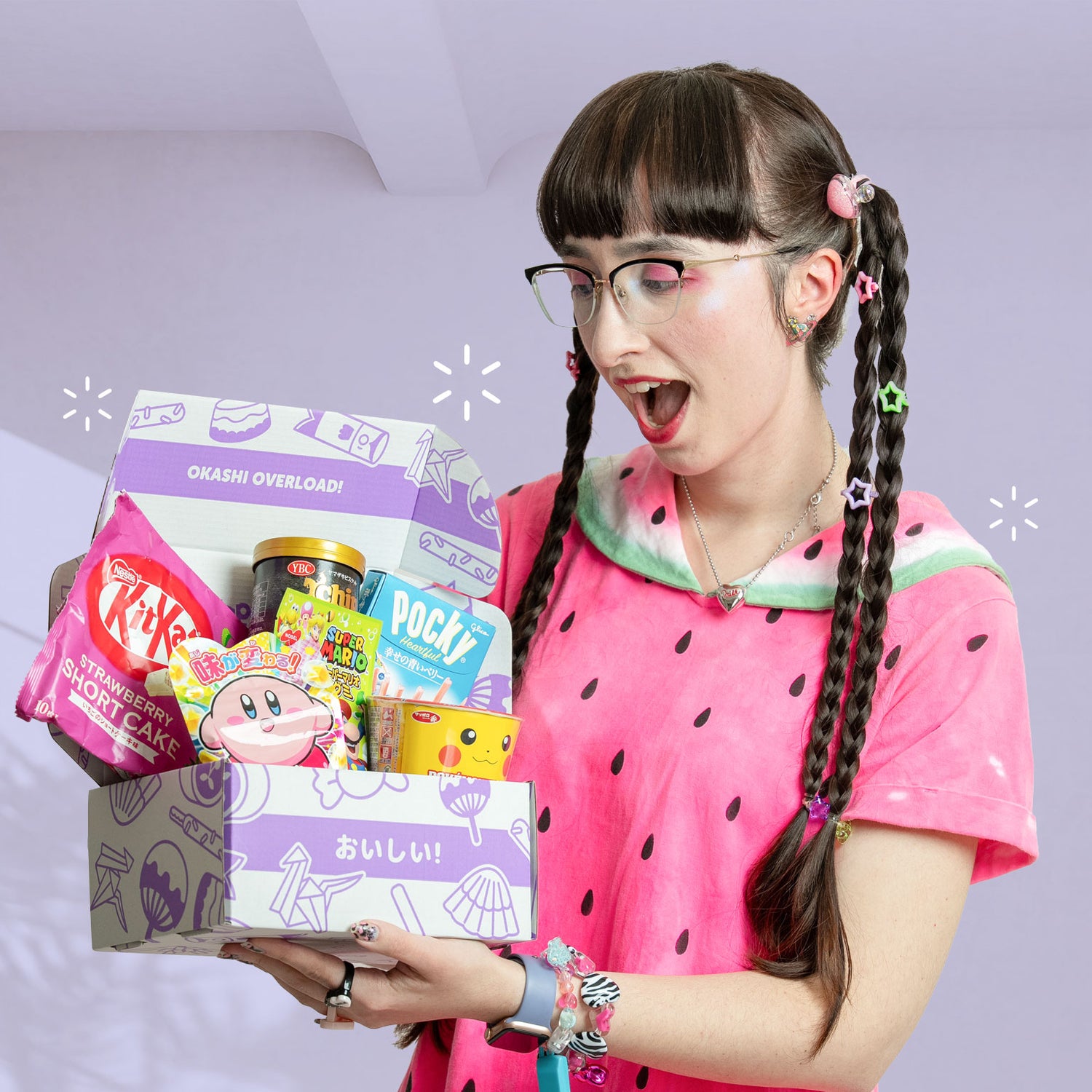 Person holding a box of snacks with KitKat and Poké,om packaging, wearing a pink watermelon-themed shirt.