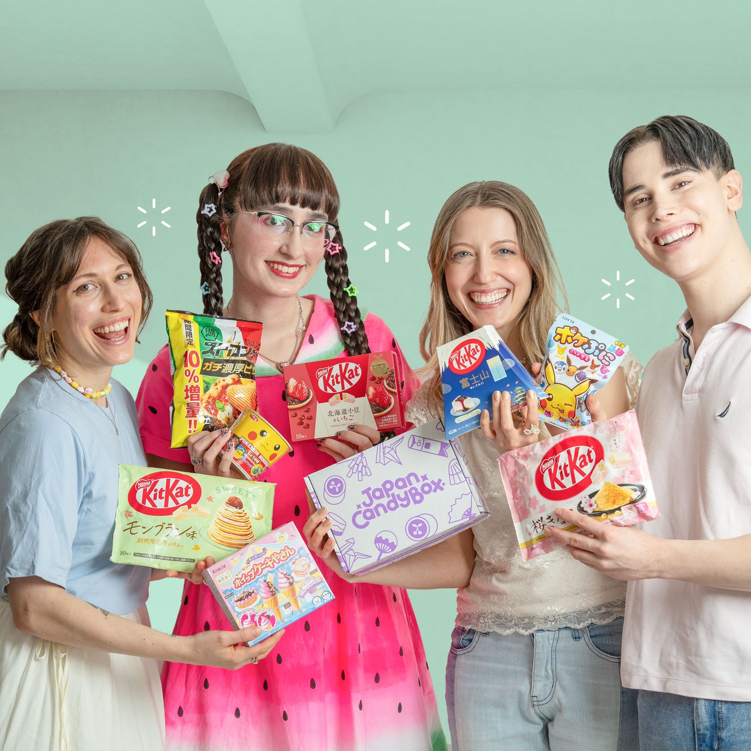 Four people holding various KitKat and Japanese candy boxes against a light green background
